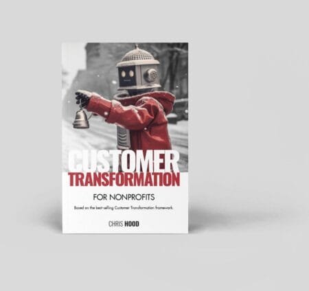 A robot with a vintage head holding a small bell, dressed in a red jacket, standing outdoors on a snowy day promoting "Customer Transformation" for nonprofits by Chris Hood.