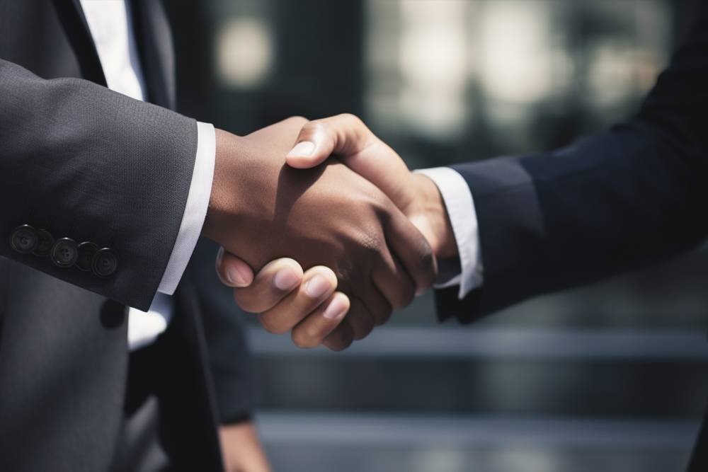 Handshake between two business professionals in formal suits symbolizing agreement or partnership, with a blurred urban background.
