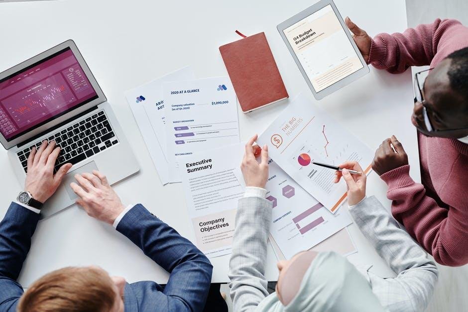 Data analysis and business meeting with financial reports on laptop and tablets, professionals discussing strategic growth and company objectives for business success.